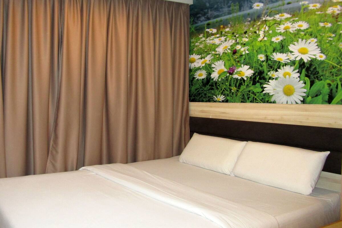 A hotel room with a bed, beige curtains, and a wall mural of daisies.