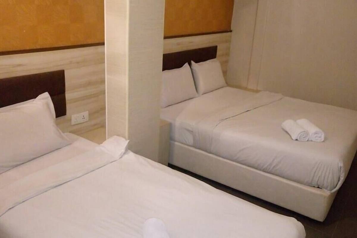 Two single beds with white linens, a wooden headboard, and a small table with rolled towels.