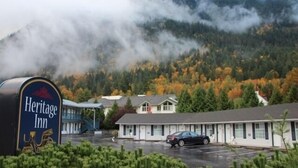 Un hotel histórico con el paisaje de montañas de fondo, un estacionamiento y un edificio de techo plano.