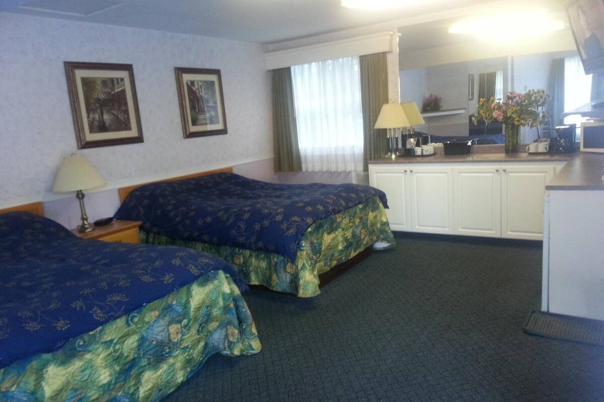 A hotel room with two beds, a desk, a mirror, and a window with curtains.
