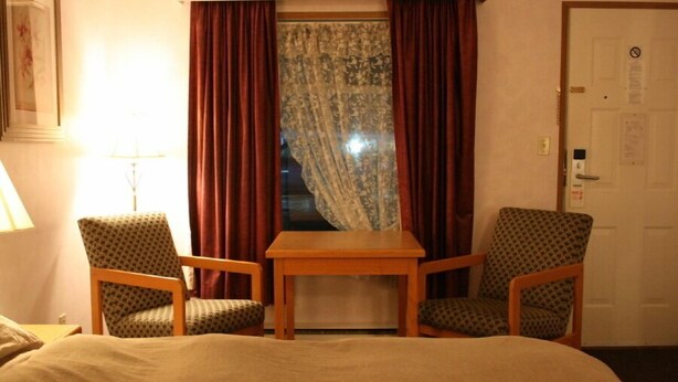 Habitación de hotel con cama, dos sillones, una mesita de madera y ventana con cortinas.