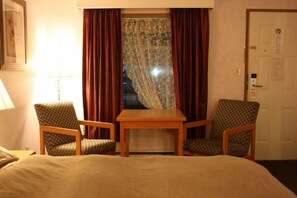 A hotel room with a bed, two armchairs, a small wooden table, and a window with curtains. - Heritage Inn (Hope)