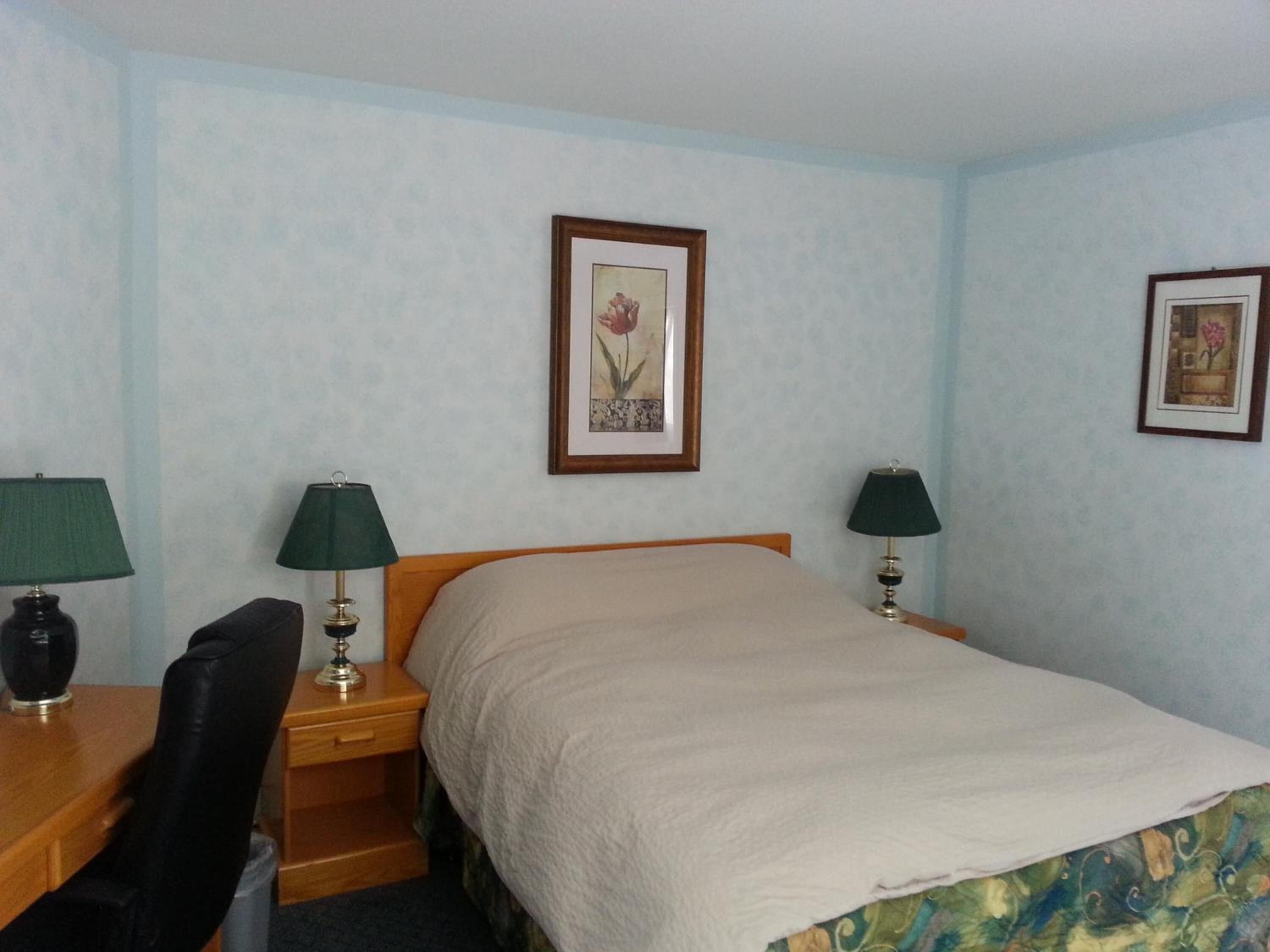 Ein Hotelzimmer mit einem Bett, zwei Nachttischen mit Lampen, einem Sessel und zwei gerahmten Bildern an der Wand.