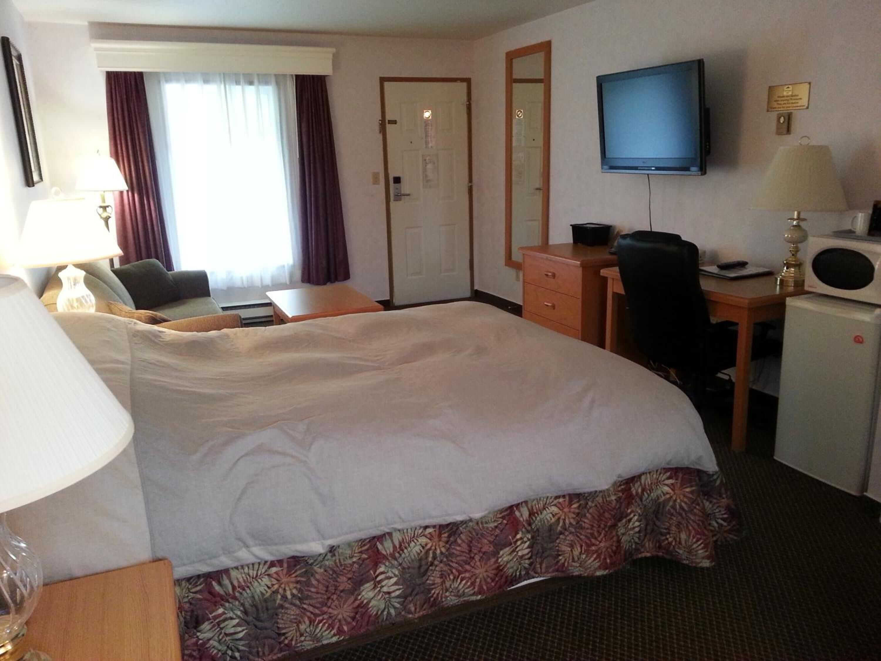 A hotel room with a large bed, a desk with a chair, a television, and a microwave.