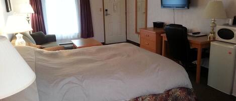 A hotel room with a large bed, a desk with a chair, a television, and a microwave.