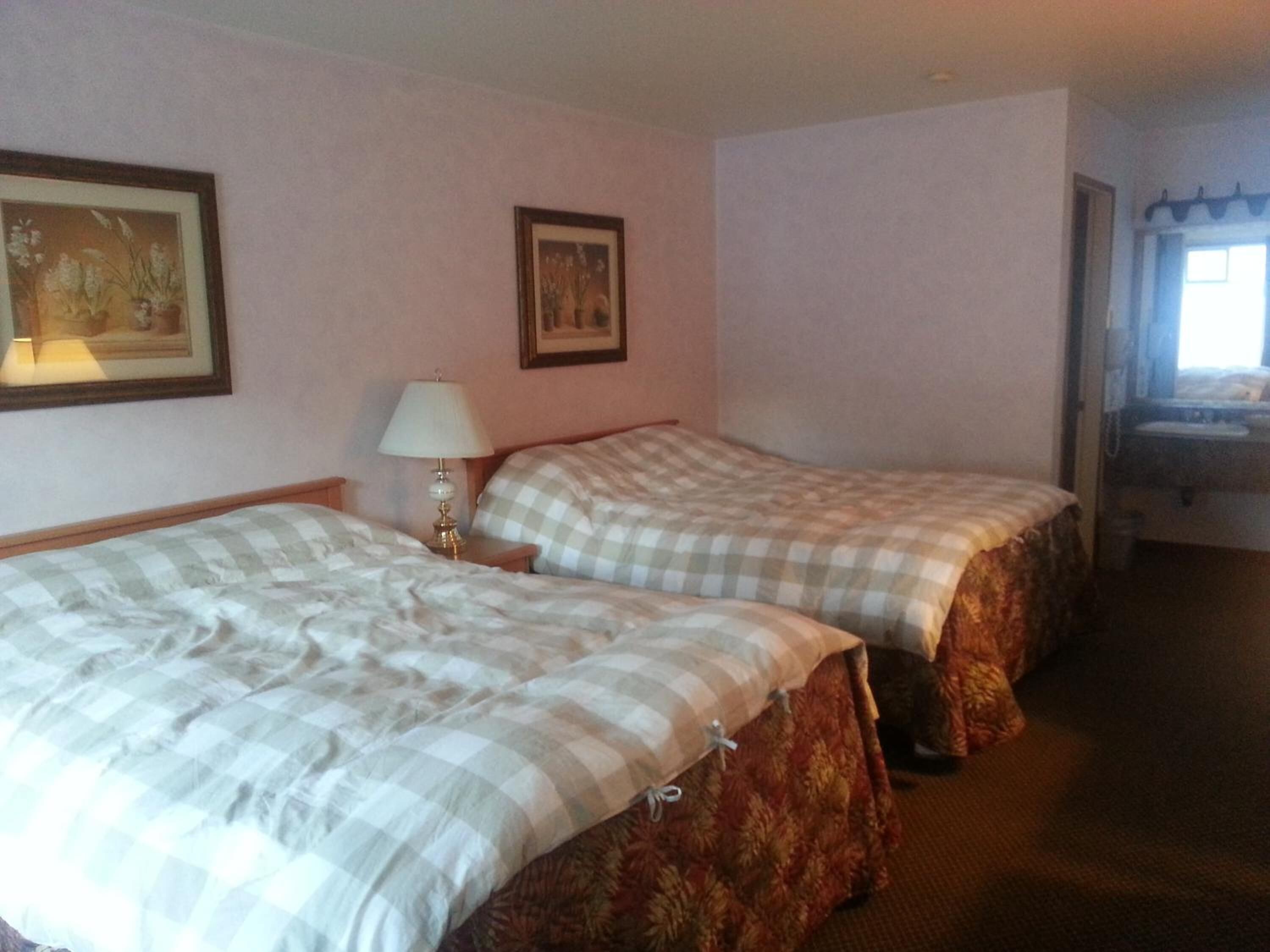 A hotel room with two beds, a nightstand with a lamp, and a framed picture on the wall.