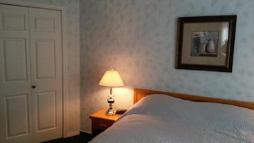 Een hotelkamer met een bed, een nachtkastje met een lamp, een lijst met een foto aan de muur en een deur.