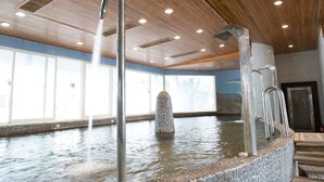 Een binnenzwembad met helder water, metalen trappen en een stenen fontein.