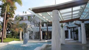 A pool with a waterfall feature, surrounded by palm trees and a covered area with columns.