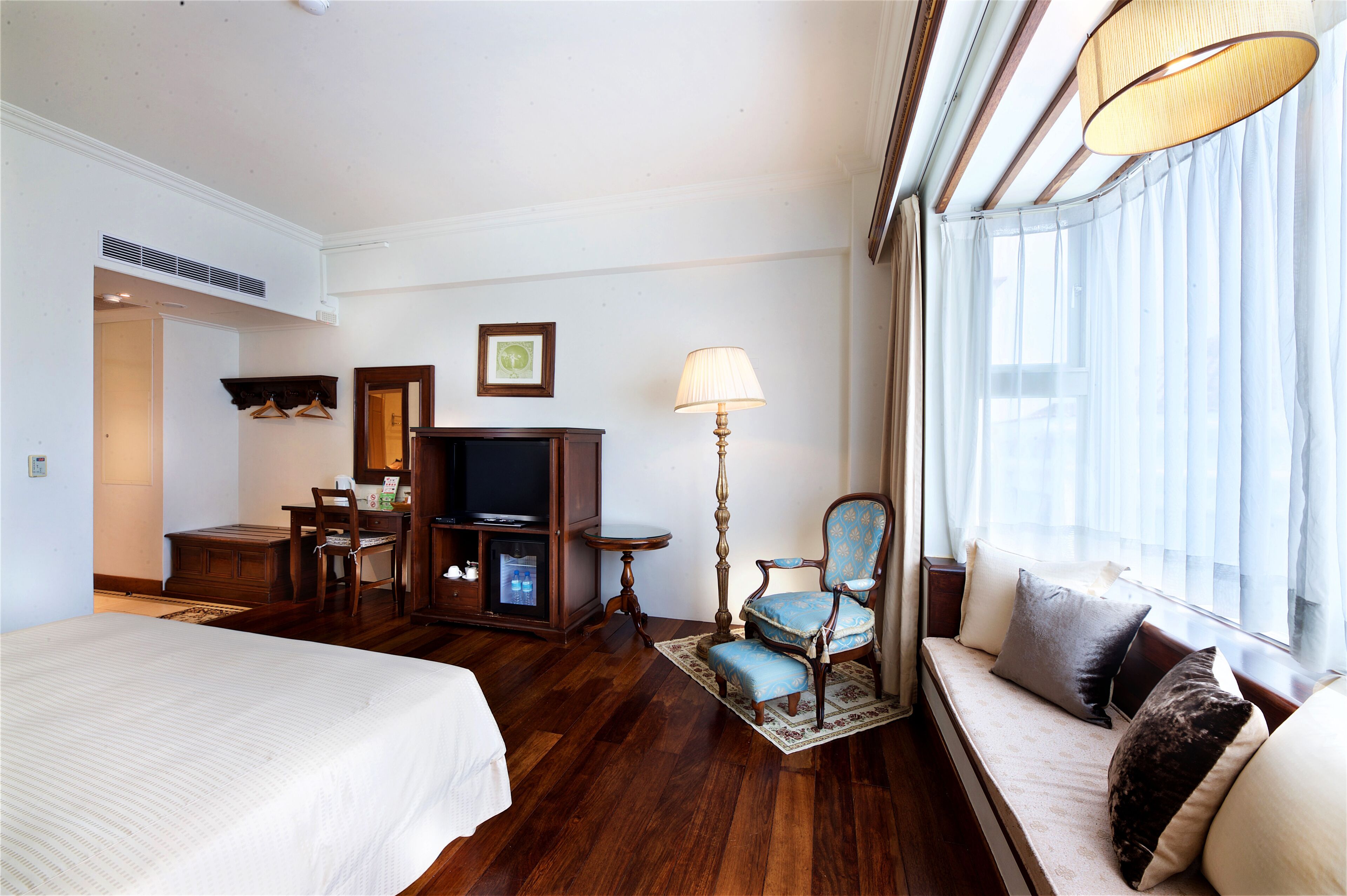 Una habitación de hotel con cama, sofá, escritorio con silla, televisión y ventana con cortinas.