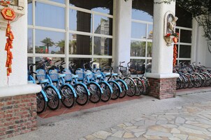 Varias bicicletas están estacionadas frente a un edificio con amplios ventanales y un columno de ladrillo.