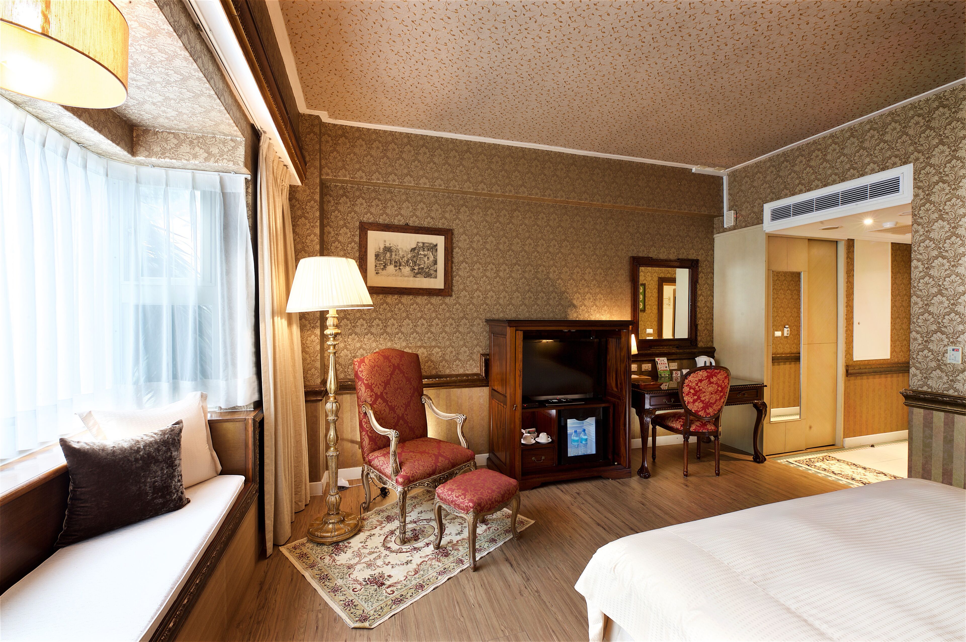 Een hotelkamer met een bed, een slaapbank, een bureau met stoel, een televisie en een grote spiegel.
