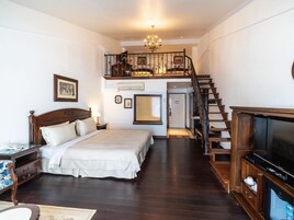 Un dormitorio con una cama grande, televisor, escalera de madera y candelabro.