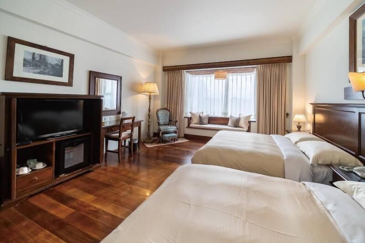 Ein Hotelzimmer mit zwei Betten, einem Fernseher, einem Schreibtisch und einem Fenster mit Vorhängen.