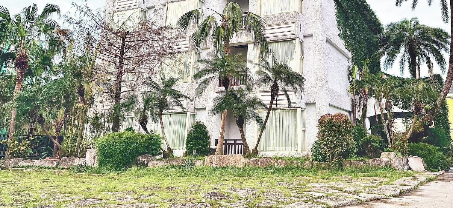 Un edificio de varios pisos con balcones, rodeado de palmeras y follaje.