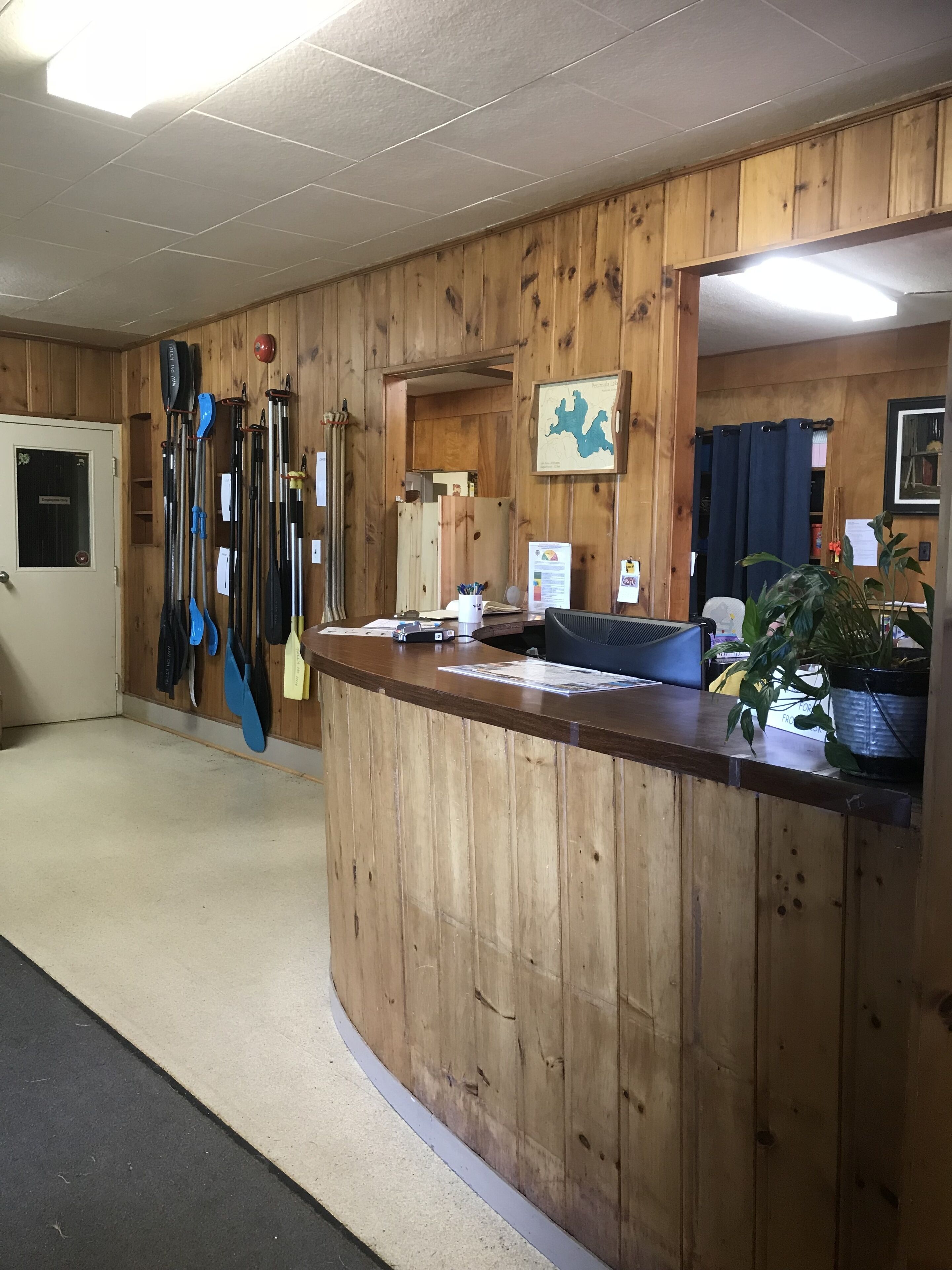 A wooden reception desk with a map on the wall, a door to the left, and a plant on the right.