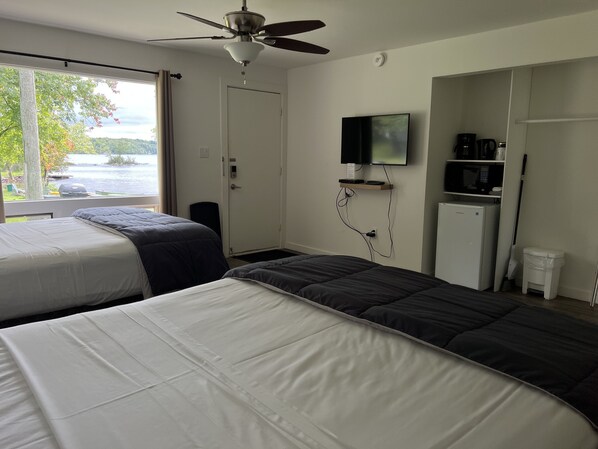 Habitación de hotel con dos camas, ventilador de techo, televisión, cafetera y vista al lago.