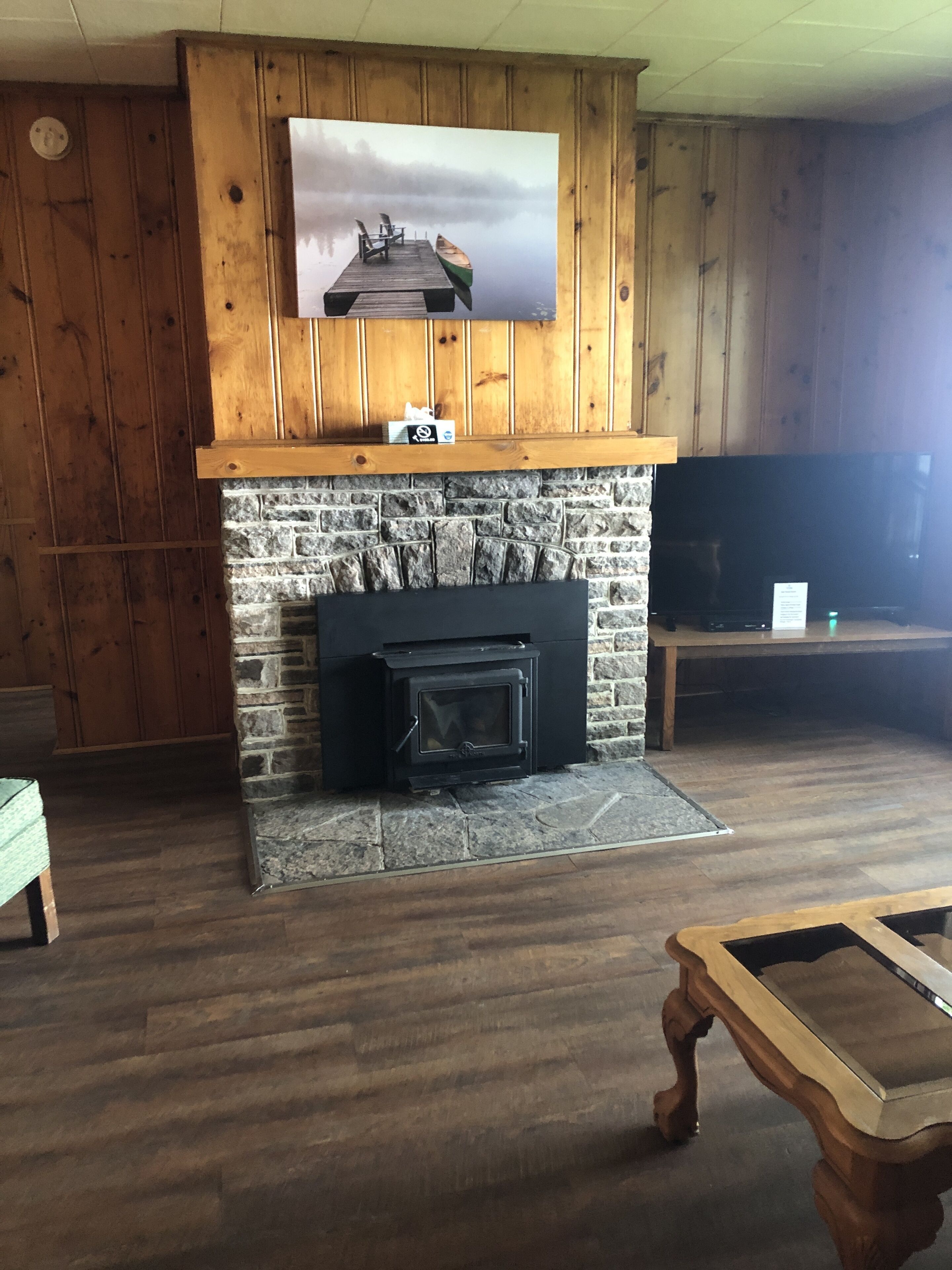 Una sala de estar con chimenea de piedra, paneles de madera en las paredes, televisor montado y mesa de centro de madera.
