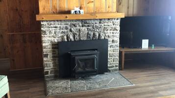 Una sala de estar con chimenea de piedra, paneles de madera en las paredes, televisor montado y mesa de centro de madera.