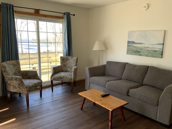 A living room with a sofa, two armchairs, a wooden coffee table, and a window with curtains.