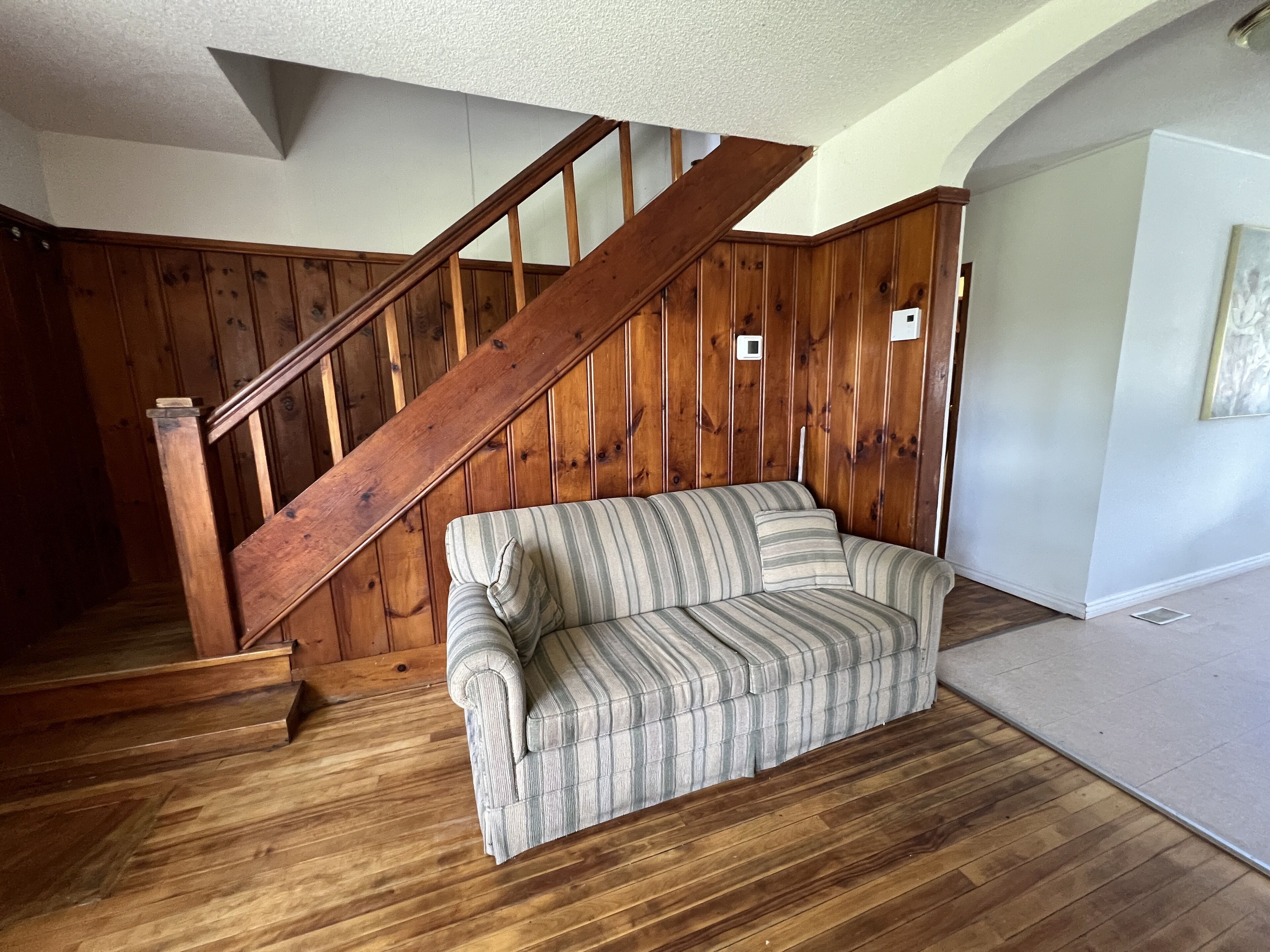 A wooden staircase with a wooden handrail, a striped sofa, and a wooden floor.