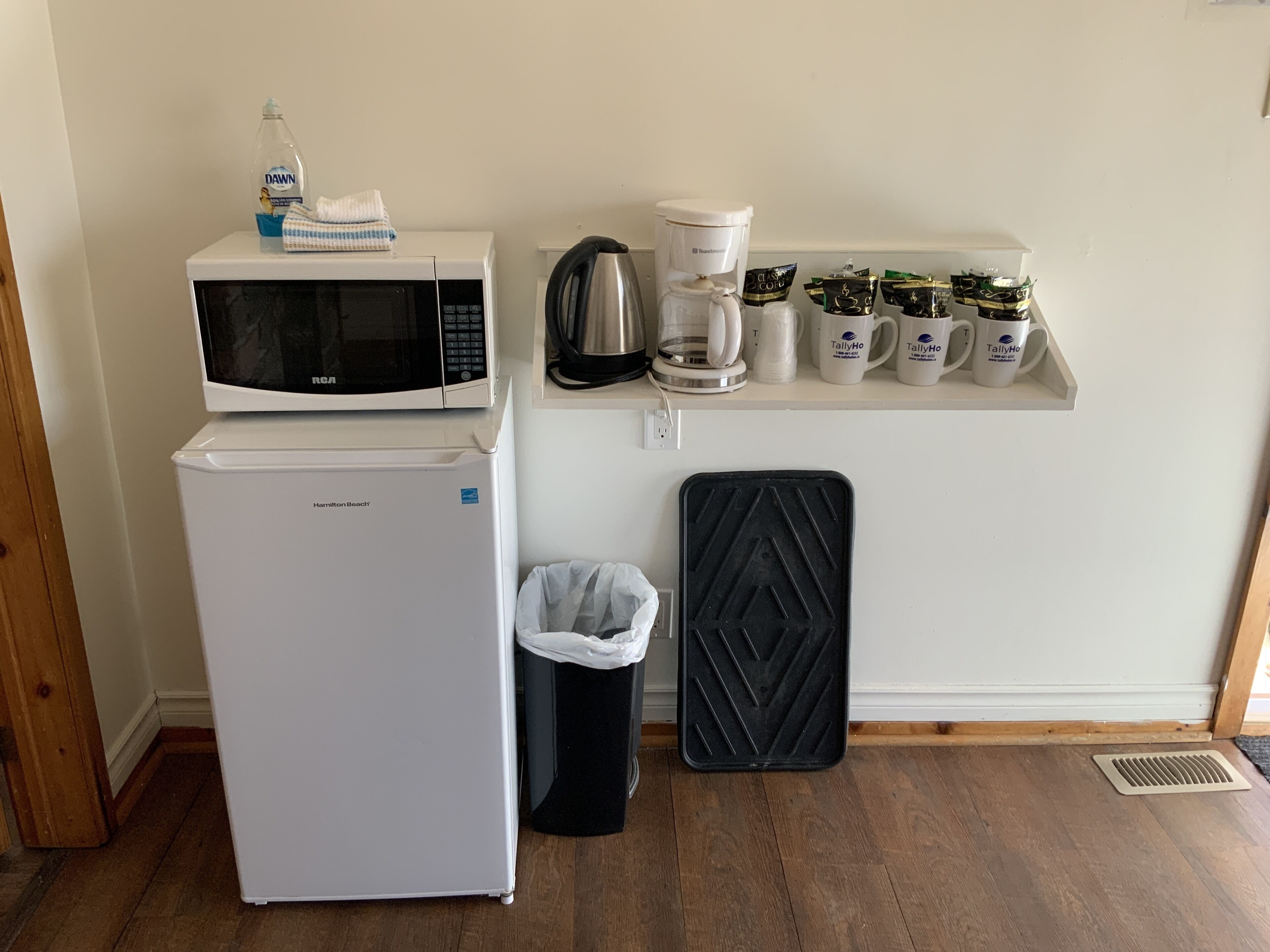 A compact kitchenette with a microwave, coffee maker, and storage mugs.