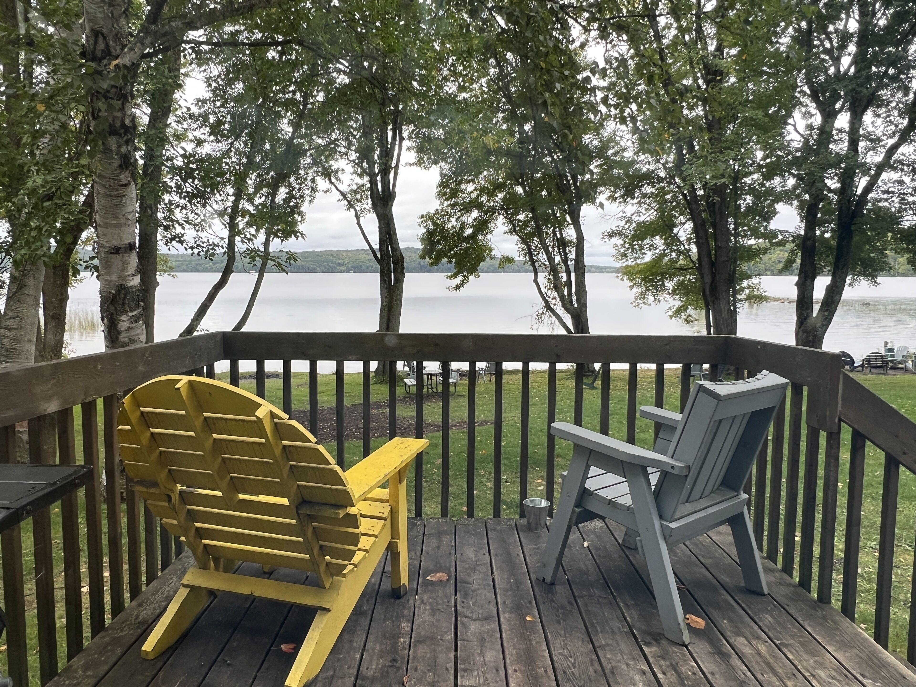 Una terraza de madera con dos sillas Adirondack mirando un lago.