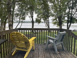 A wooden deck with two Adirondack chairs facing a lake.
