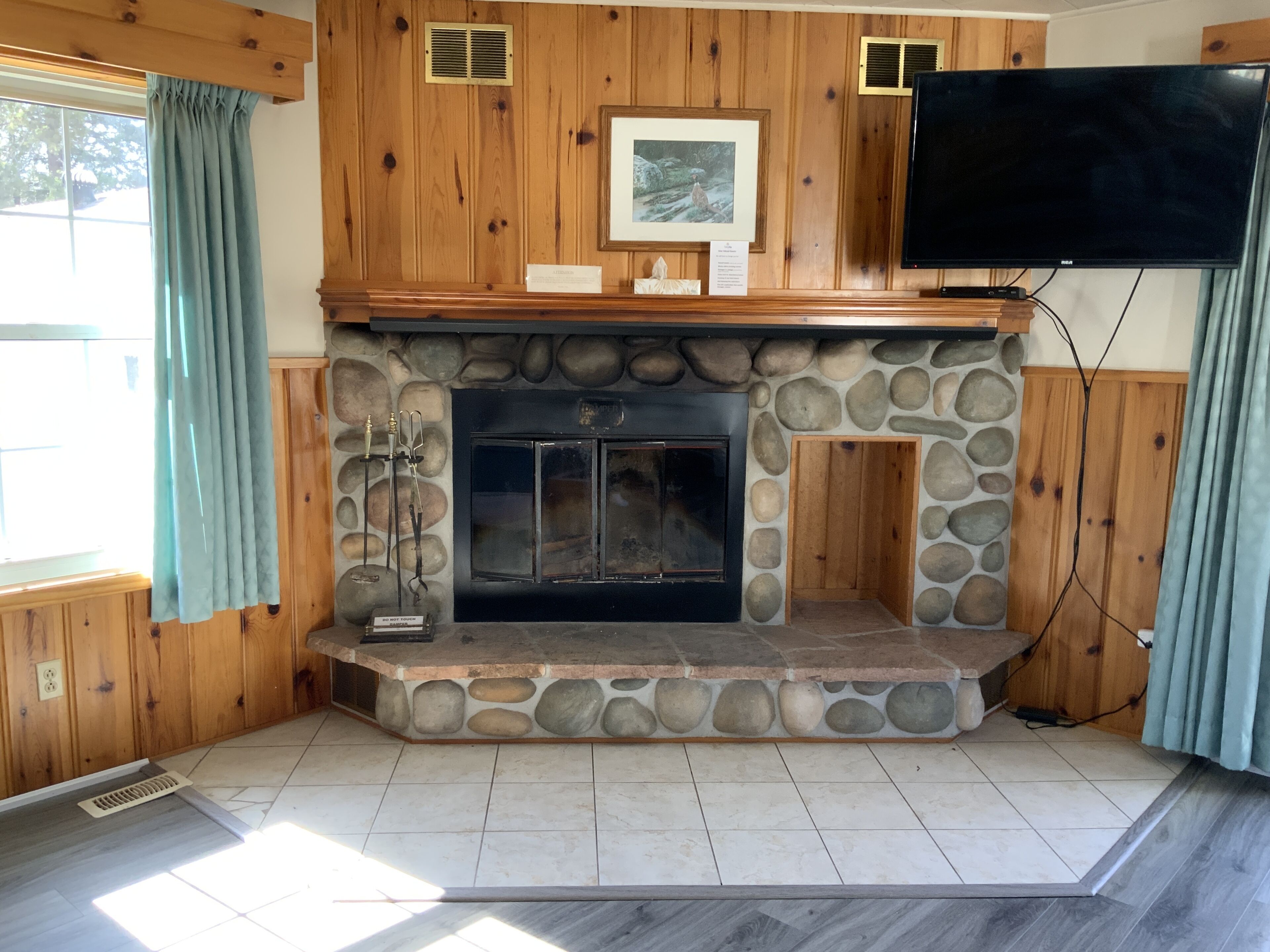 A stone fireplace with a TV mounted above it, set in a wooden-paneled room with a stone accent wall.