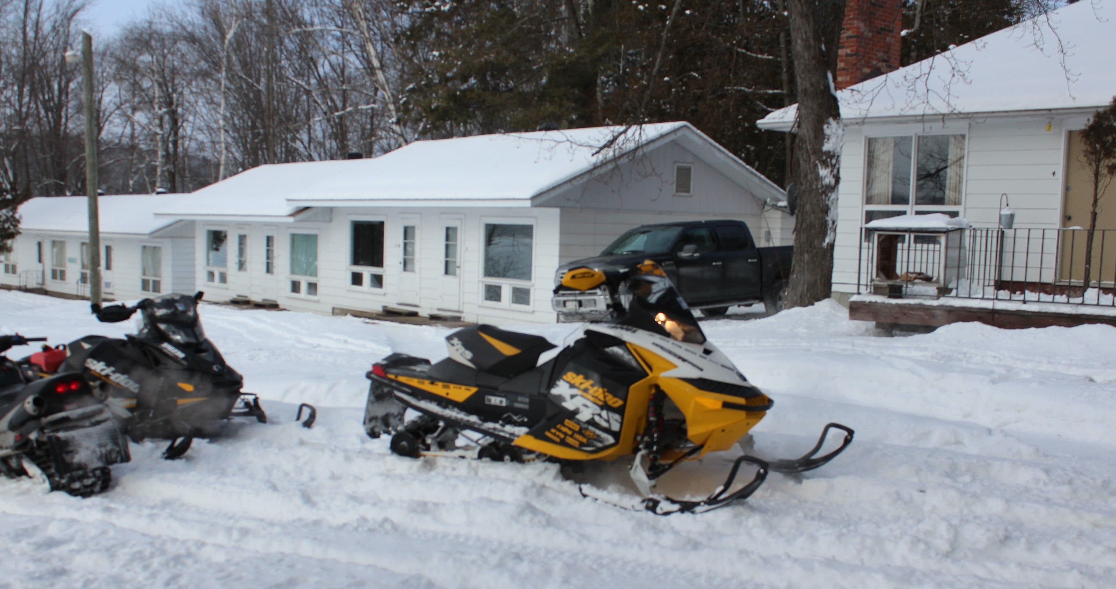 Two snowmobiles parked in a snowy area with houses in the background.