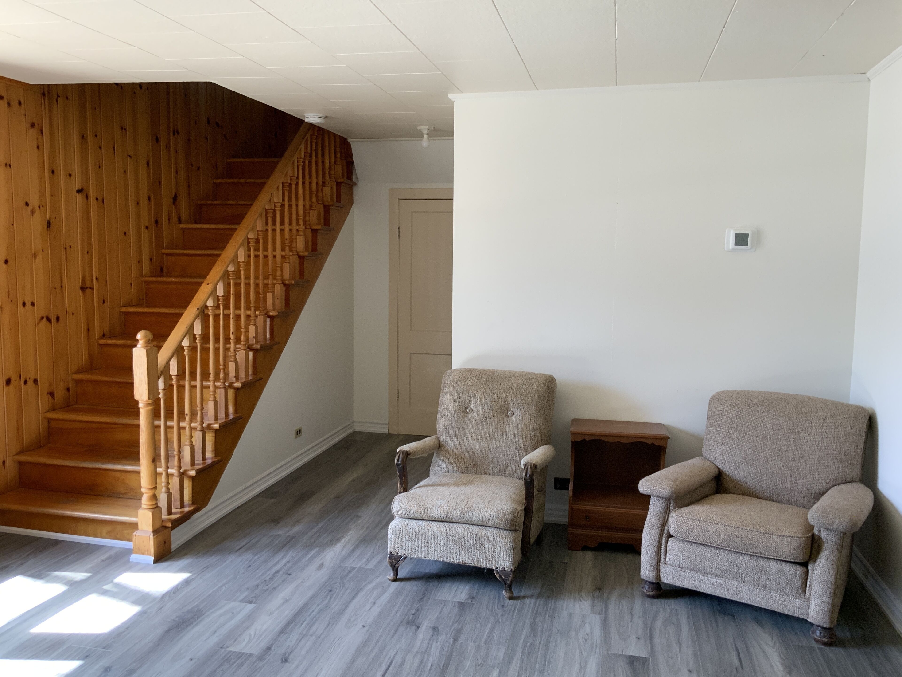Een kamer met een houten trap, twee fauteuils, een klein houten tafeltje en een witte deur.