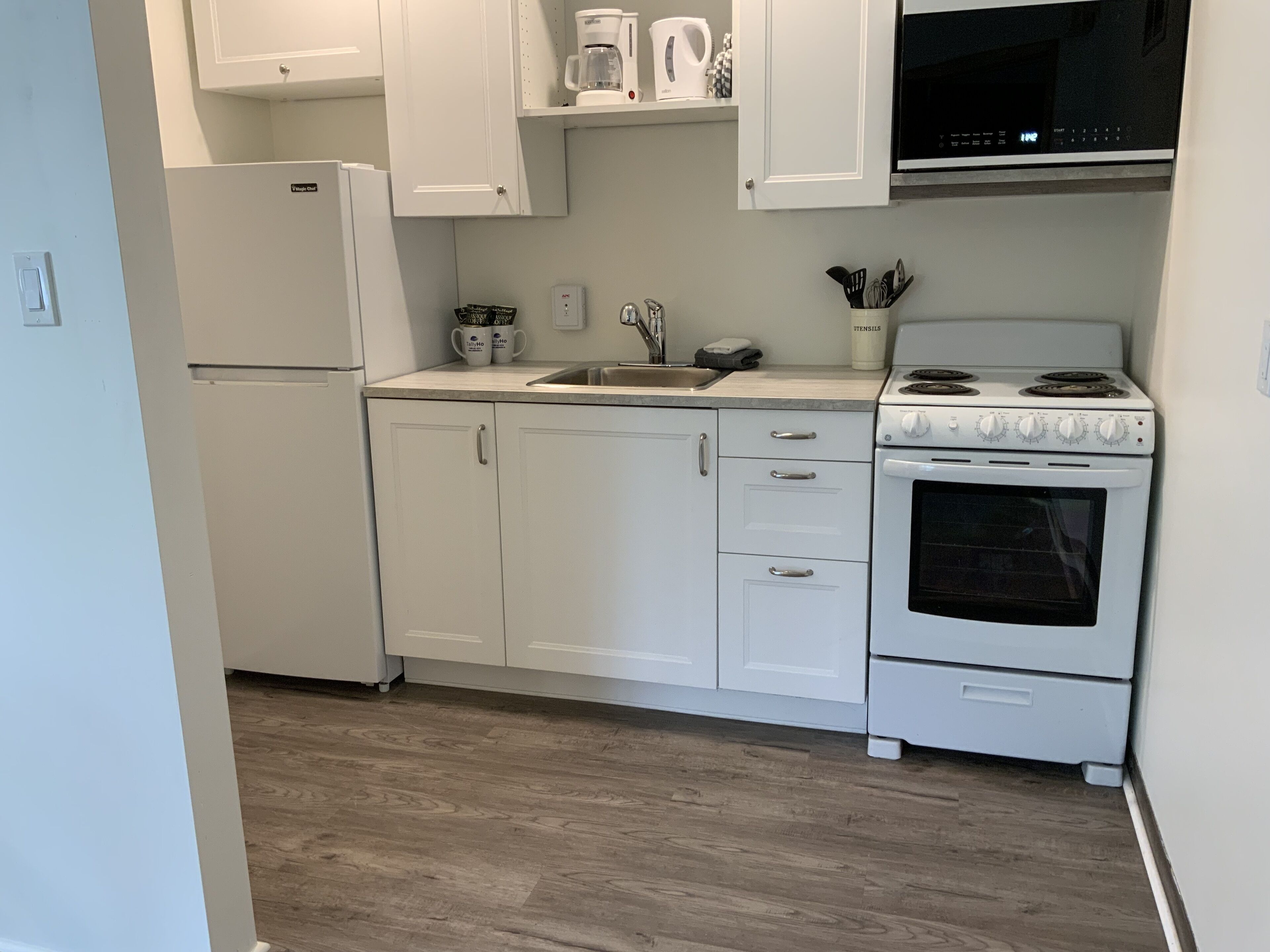 Una cocina con armarios blancos, un refrigerador, una estufa y un microondas.