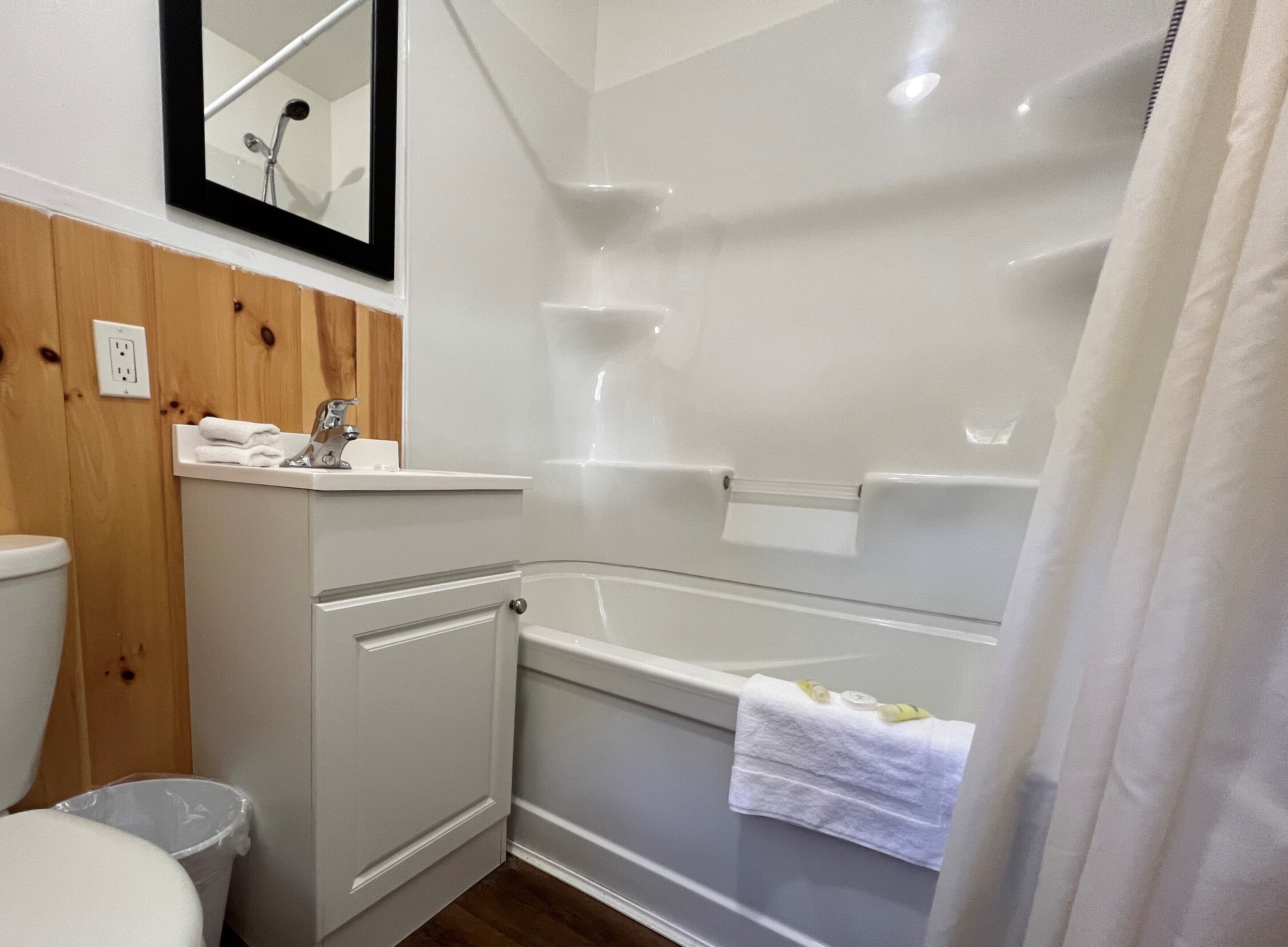 A bathroom with a white bathtub, a sink, and a toilet. There is a mirror above the sink, and a towel is hanging on the side of the bathtub.