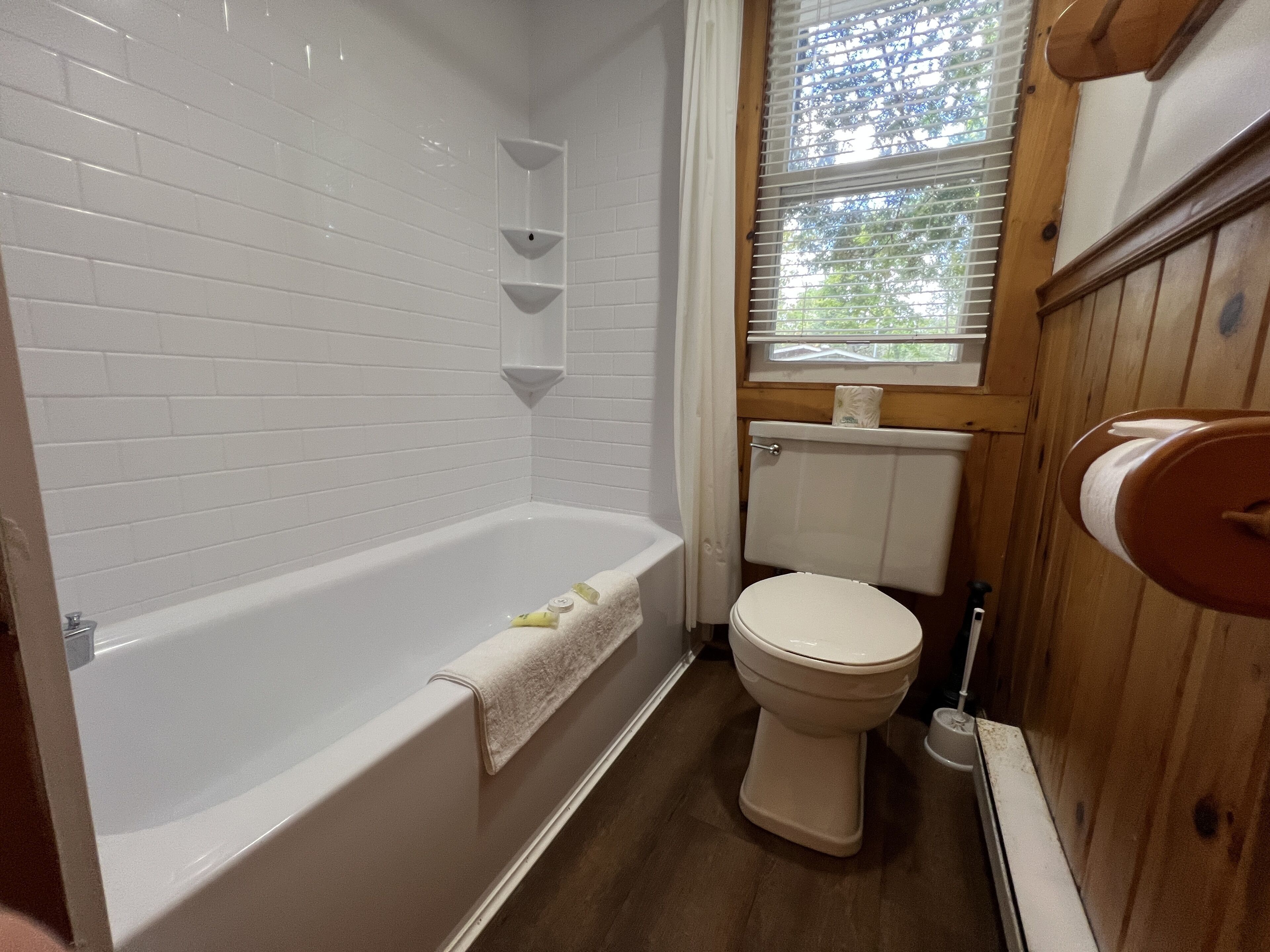 Un baño con una bañera blanca, un inodoro y una ventana con persianas.