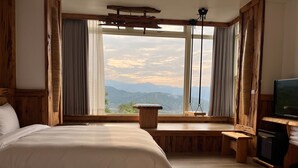 Een slaapkamer met een groot bed, een houten bankje, een televisie en uitzicht op bergen door een groot raam.