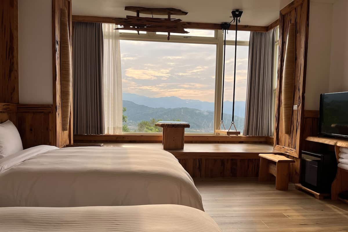 Een slaapkamer met een groot bed, een houten bankje, een televisie en uitzicht op bergen door een groot raam.