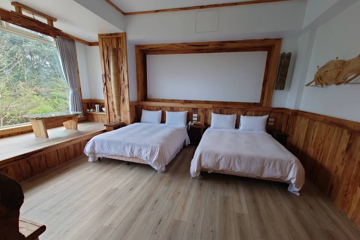 Een kamer met twee bedden, houten vloeren, een groot raam en uitzicht op groen.