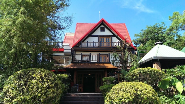 Stunning two-story building with a red roof and white facade, set amidst lush greenery and a balcony on the upper floor.