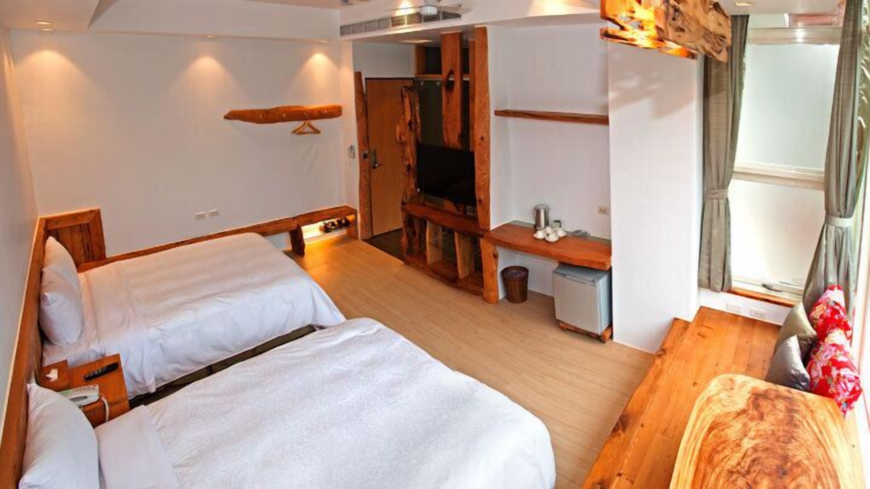Une chambre avec deux lits, un bureau en bois, une télévision et une petite kitchenette.