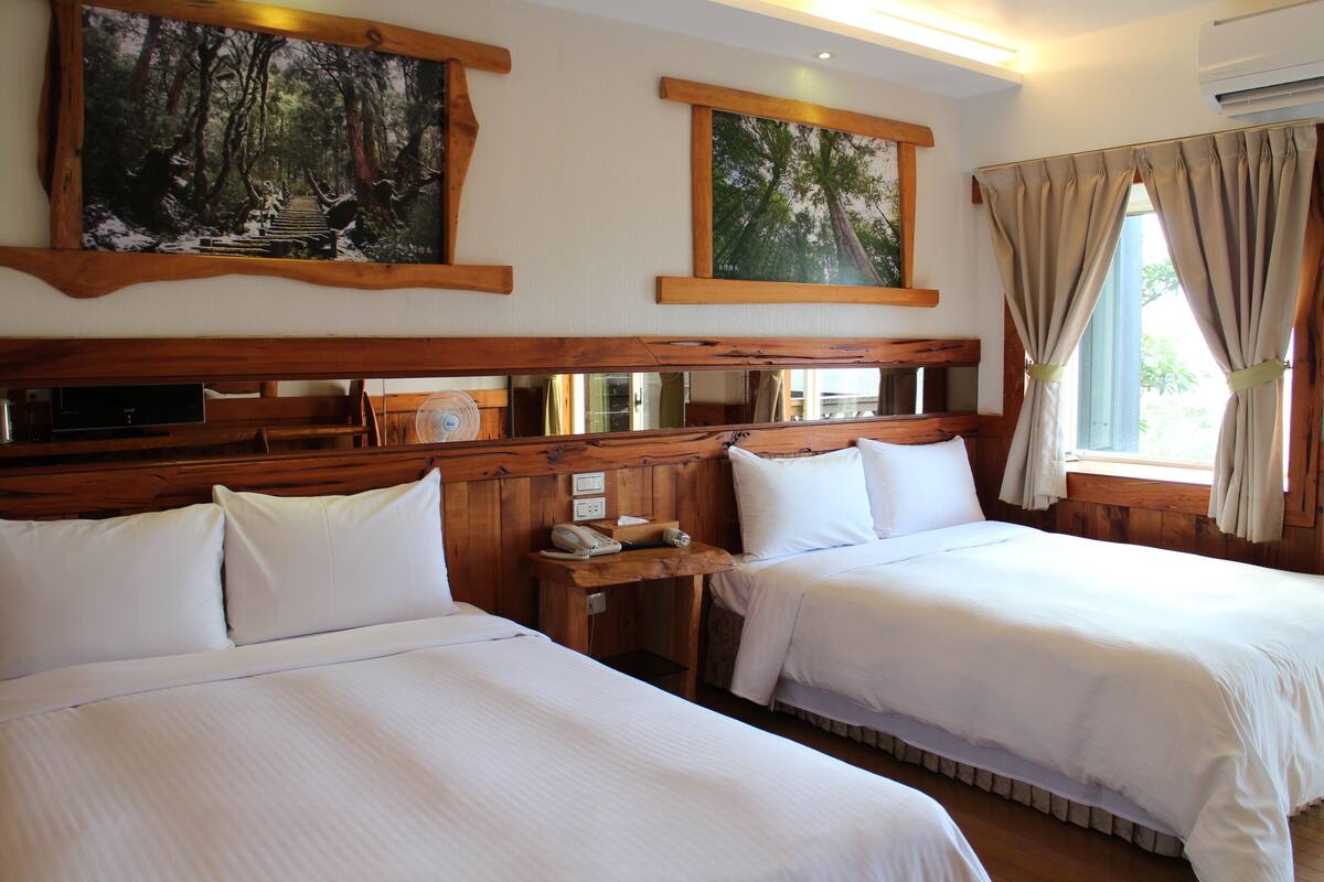 Een hotelkamer met twee bedden, een houten hoofdbord, kunst aan de muur, een tafeltje met een telefoon en een raam met gordijnen.