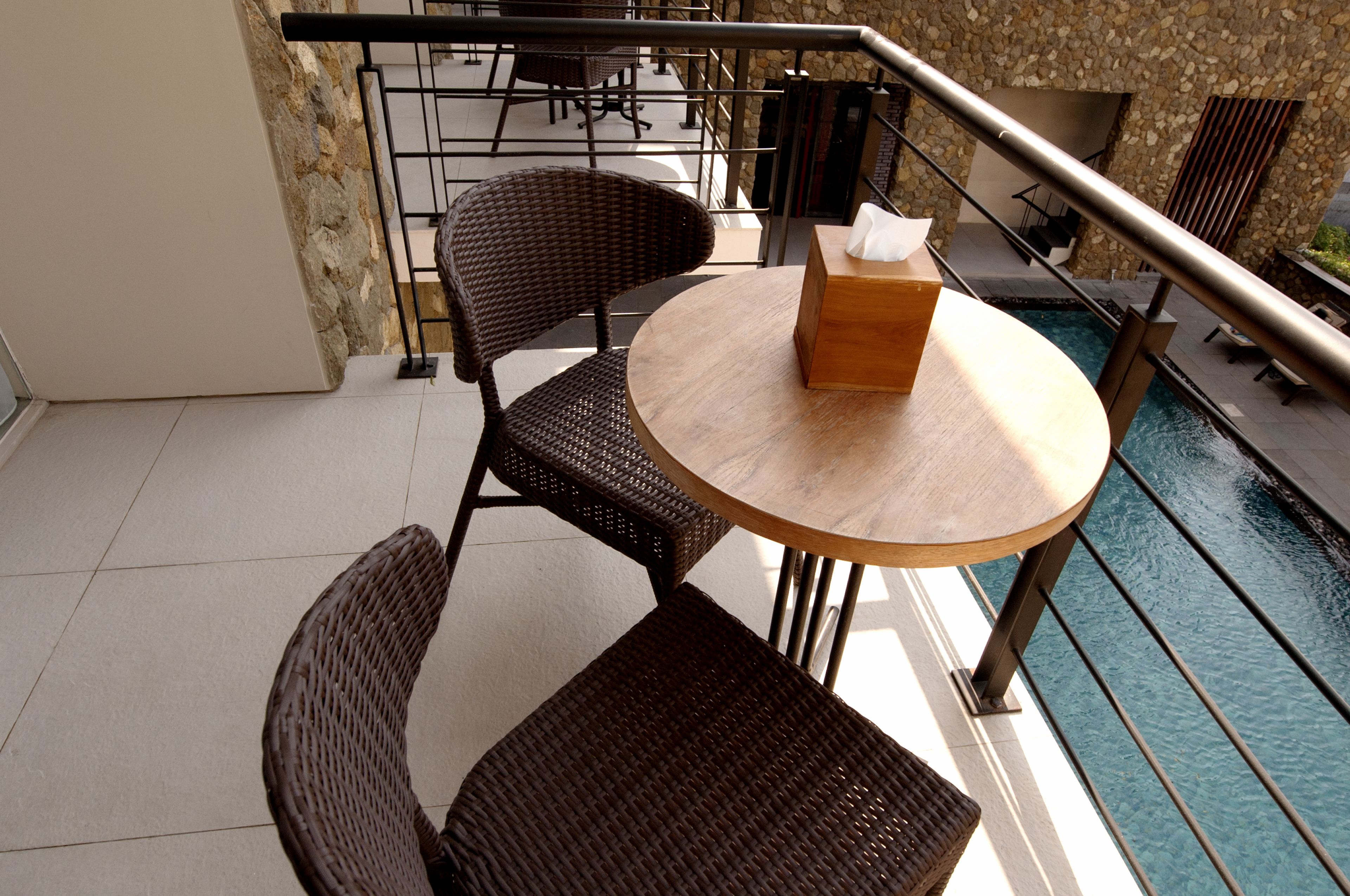 A balcony with wicker chairs, a wooden table, and a box of tissues.