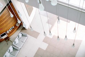 A modern hotel lobby with a wooden reception desk, a seating area with white sofas, and hanging pendant lights.