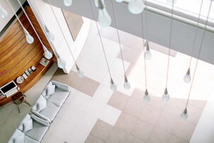 Un moderno vestíbulo de hotel con un mostrador de recepción de madera, una zona de estar con sofás blancos y lámparas colgantes.