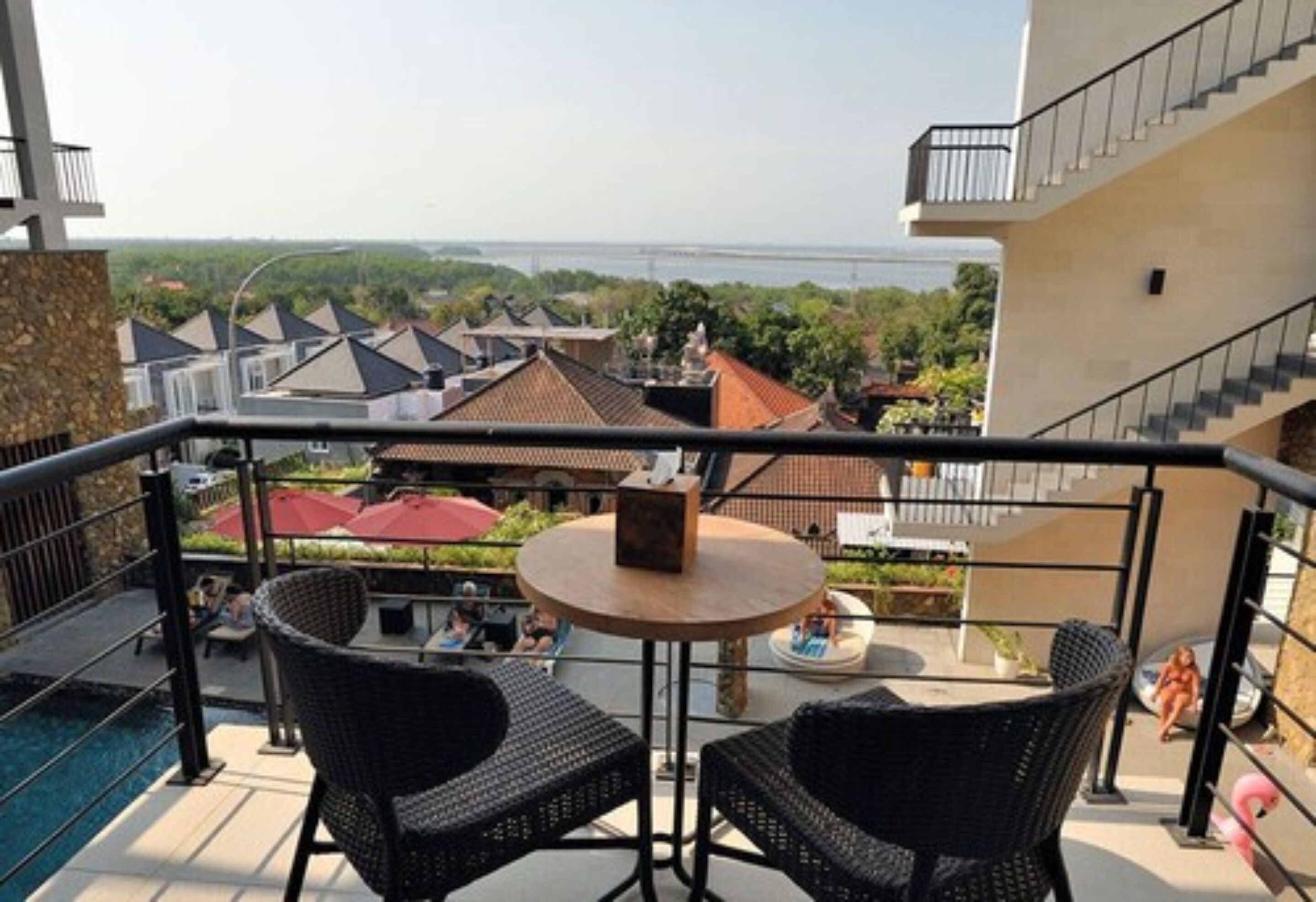 Un balcon avec des fauteuils en osier, une table ronde et une vue sur un pont et des immeubles.