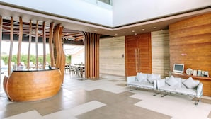 A spacious lobby with a modern reception desk, a large wooden sculpture, and a seating area with white sofas. - Mahogany Hotel (Nusa Dua)