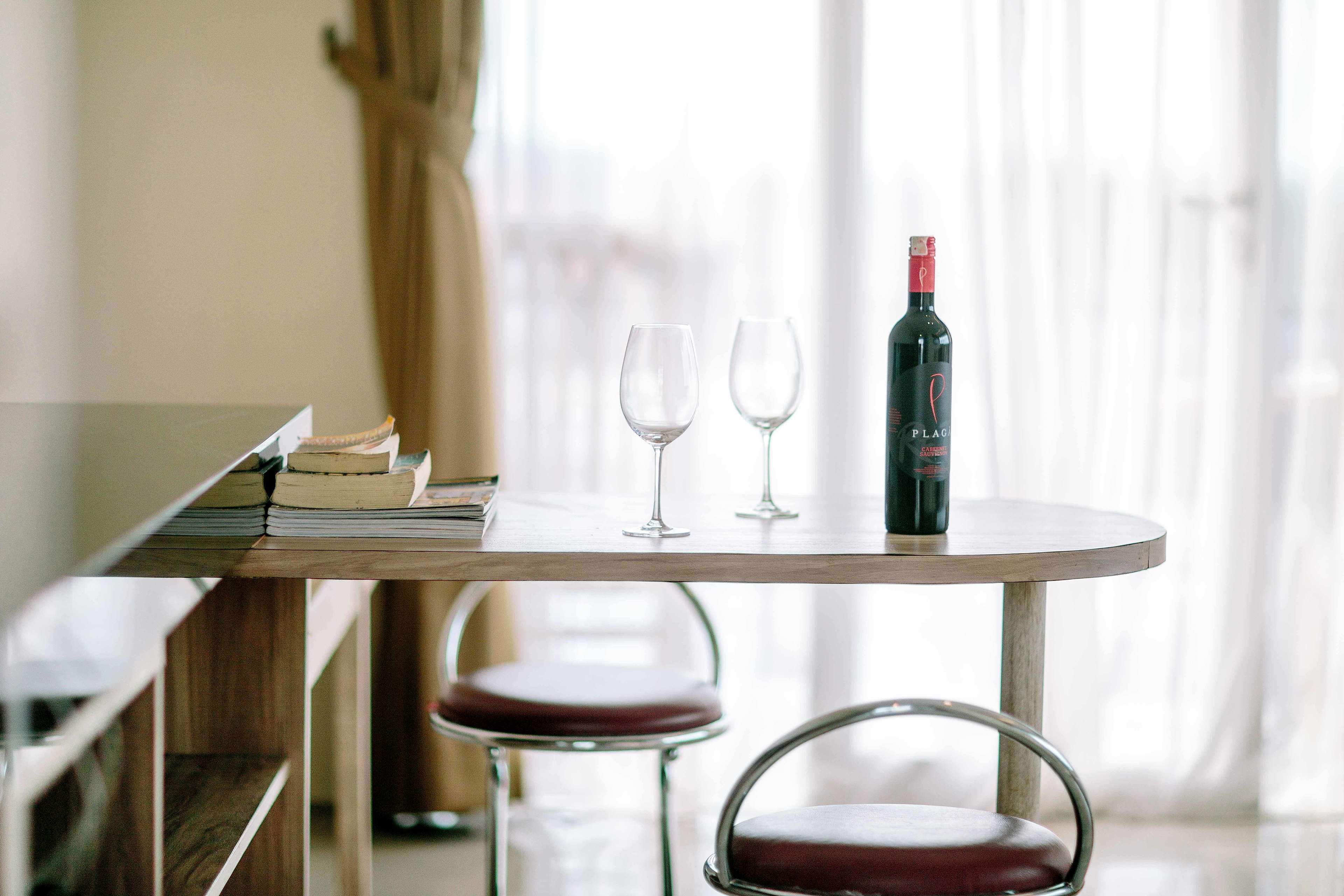 A table with a bottle of wine, two glasses, and a stack of books.