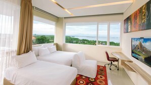 A hotel room with two beds, a desk, a chair, and a large window offering a view of a body of water and greenery. - Mahogany Hotel (Nusa Dua)