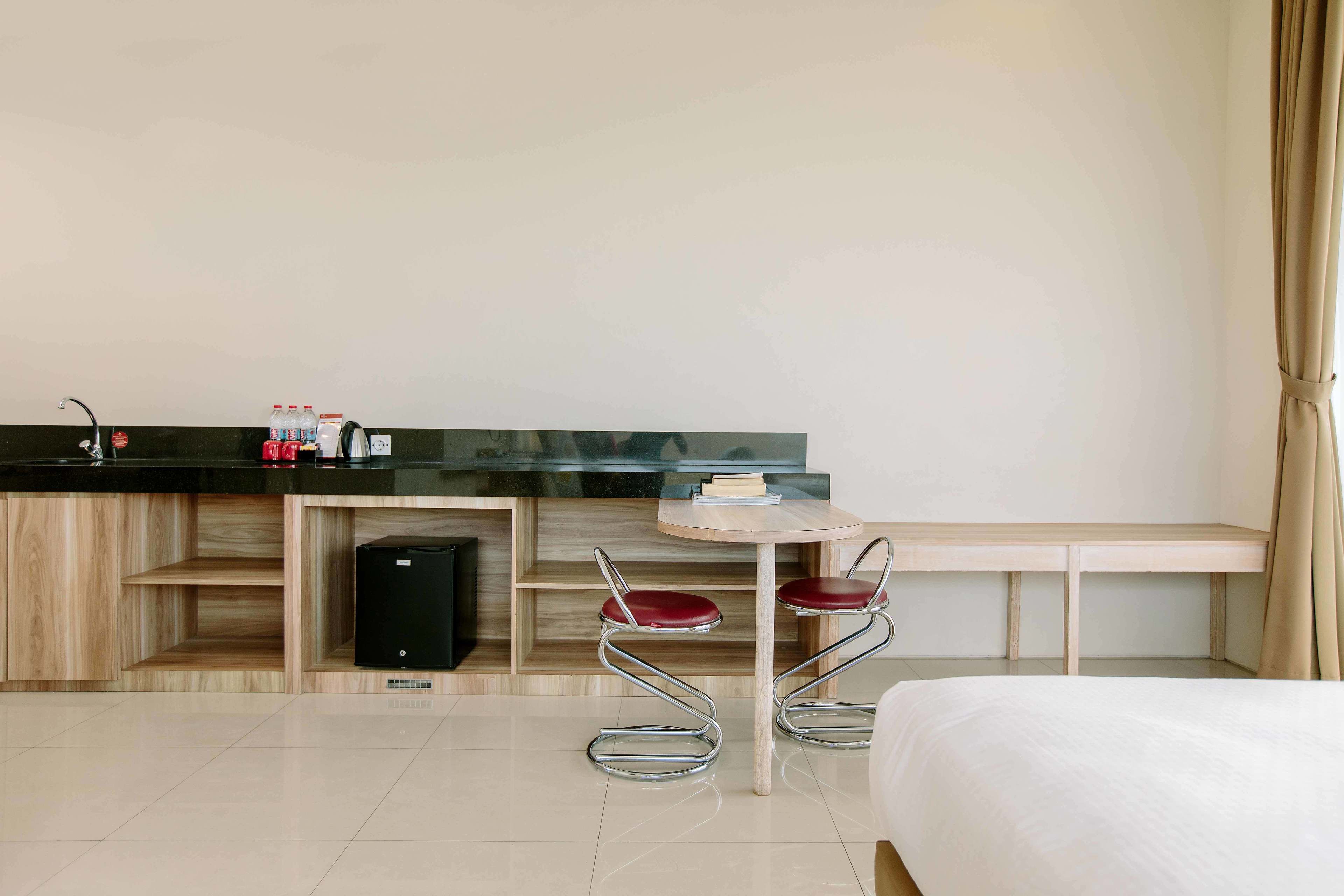 A modern hotel room with a bed, a small kitchenette, a round table with two chairs, and a built-in bench.