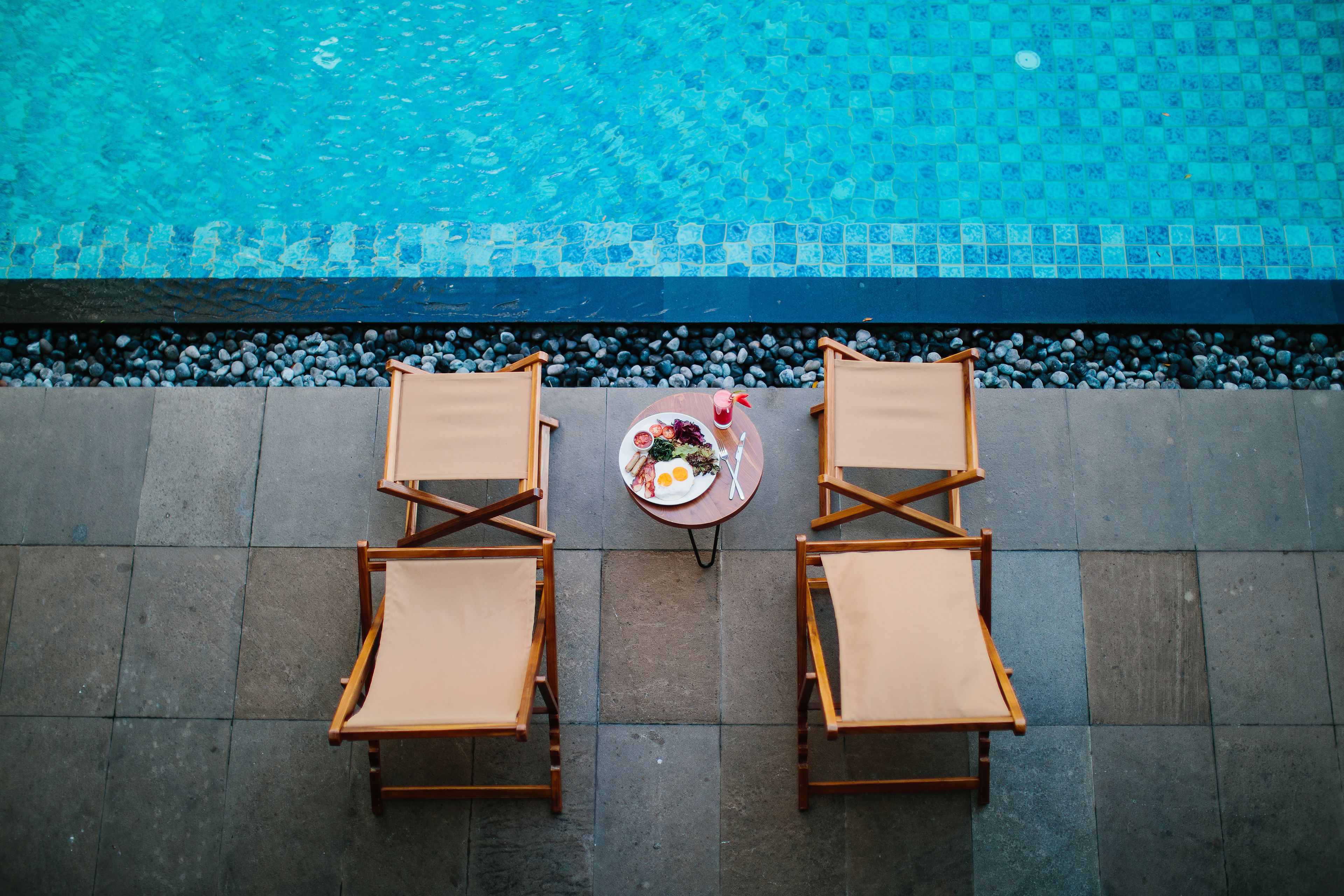 A poolside view with two lounge chairs and a table with a meal.