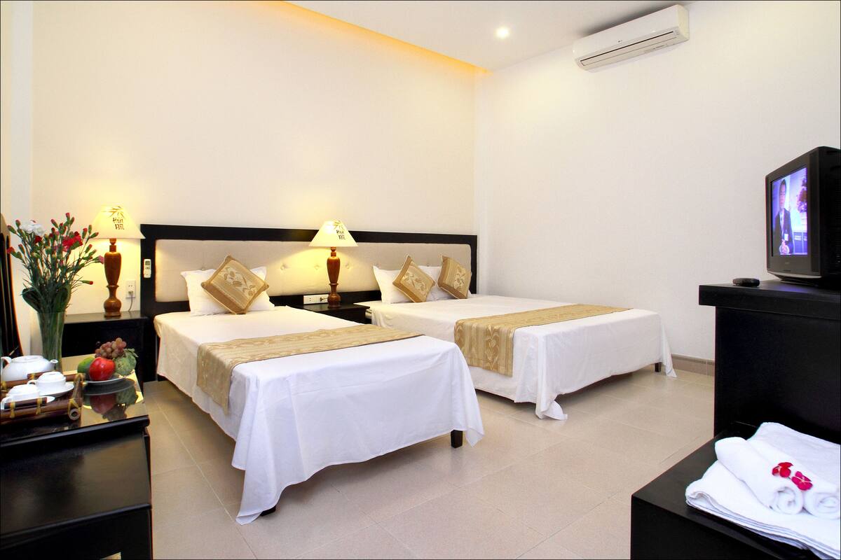 A hotel room with two beds, a TV, a desk with a lamp, and a vase with flowers.
